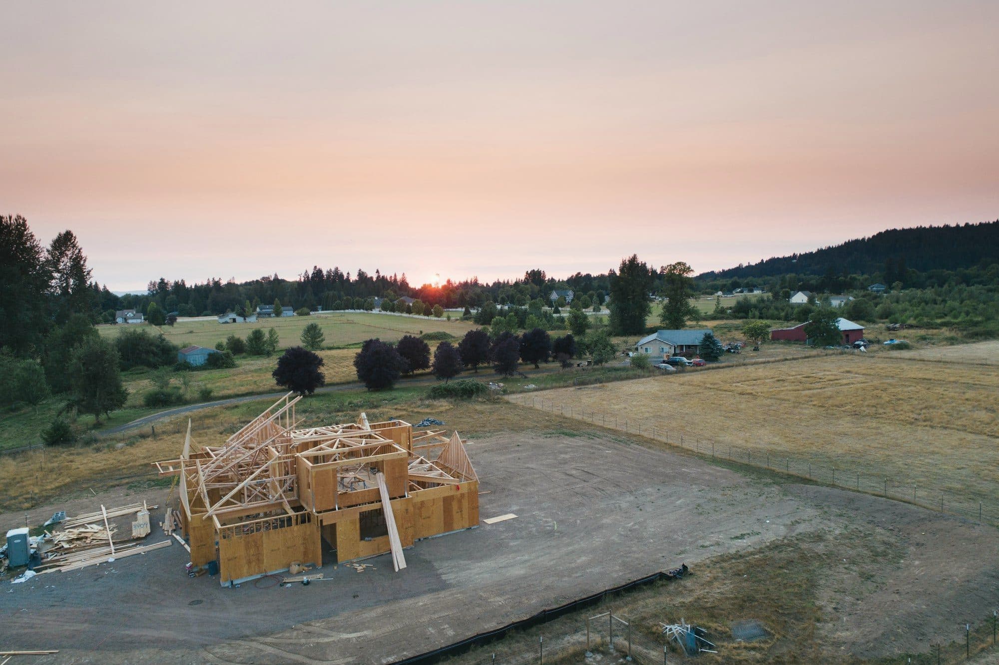 Aerial view of a new house in timber framing on an open rural lot at sunset.
